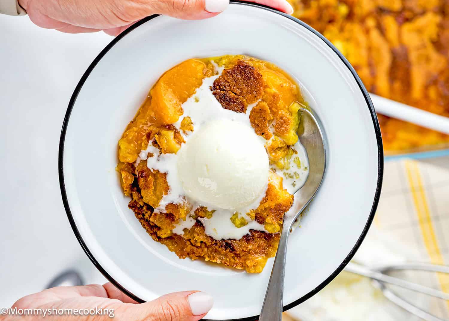 A bowl of Ultimate Easy Peach Dump Cake (5 Ingredients) topped with a scoop of vanilla ice cream, served with a spoon.