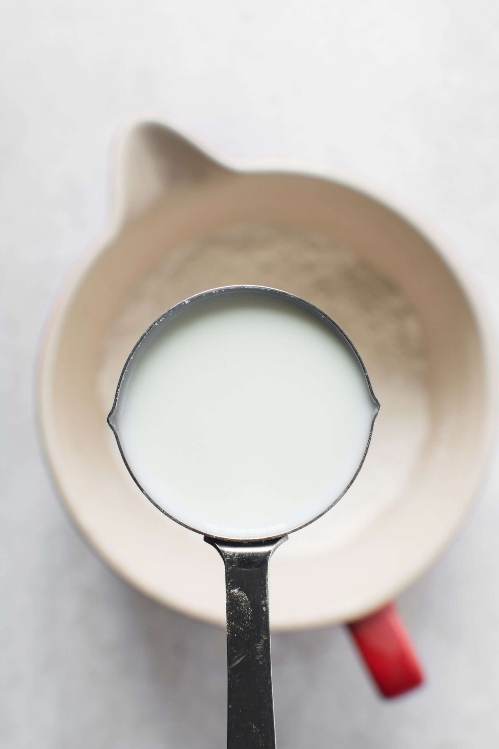 A metal measuring cup filled with milk is held above a mixing bowl of flour—perfect for trying Your Guide to Dairy-Free Swaps: How I Replace Dairy in My Family’s Egg-Free Recipes.
