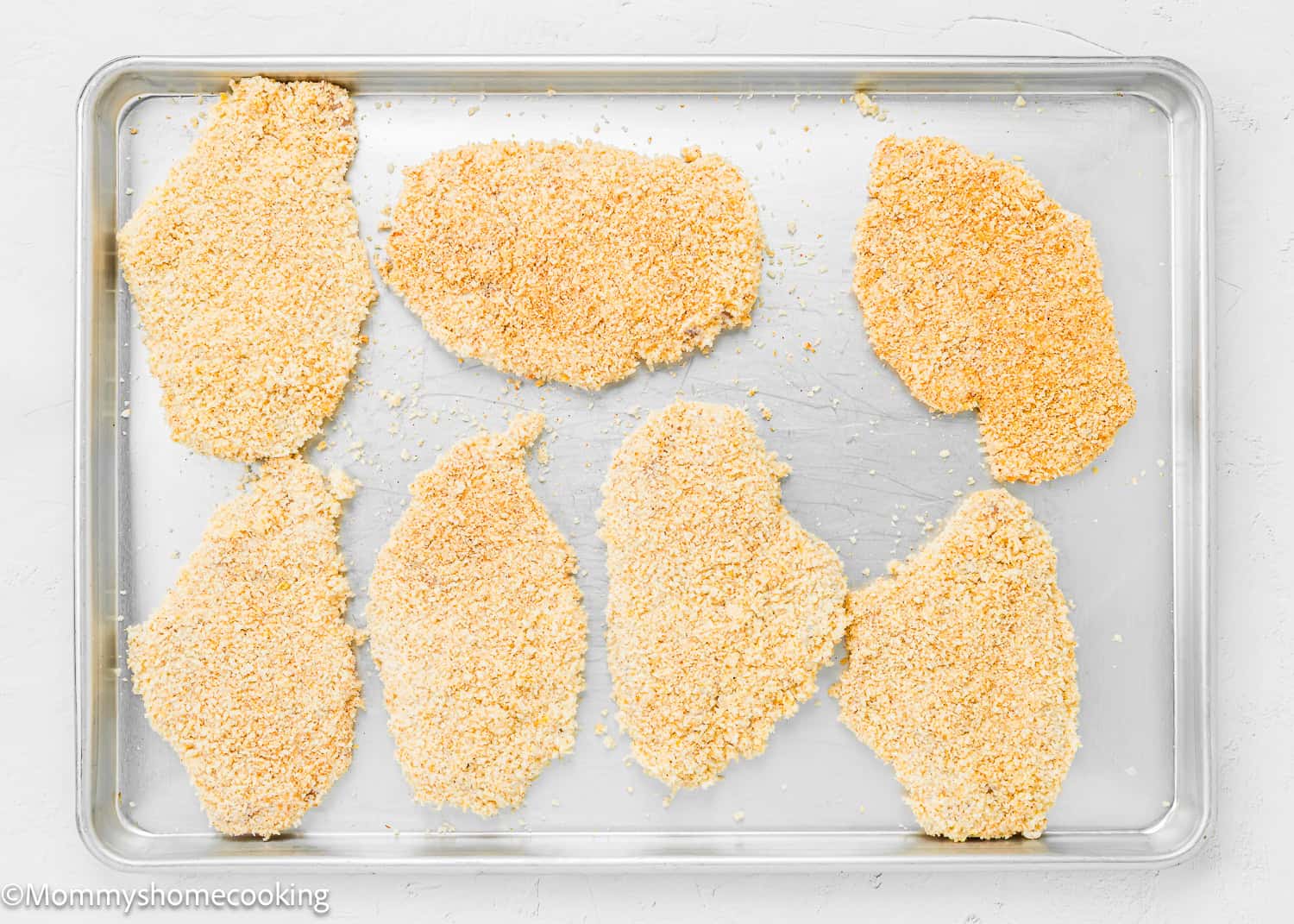 Chicken Parmesan without Eggs cutlets arranged on a metal baking sheet, ready to be cooked.