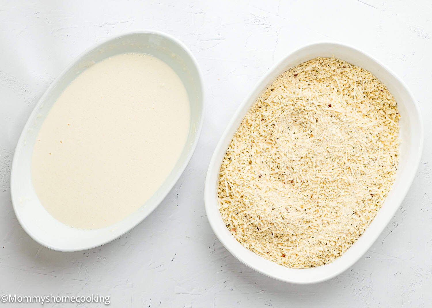 Two white oval dishes: one with creamy batter for Chicken Parmesan without Eggs, the other filled with a dry breadcrumb and grated cheese mixture, on a white surface.