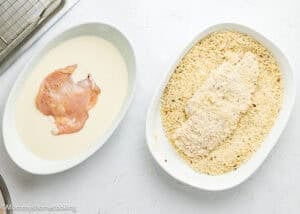 A raw chicken breast in a bowl of batter and another being coated with breadcrumbs, showing how to prepare Chicken Parmesan without Eggs.