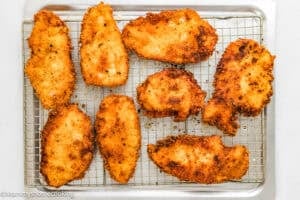 Eight pieces of golden-brown breaded and fried chicken cutlets on a wire rack over a baking tray, ideal for making Chicken Parmesan without Eggs.