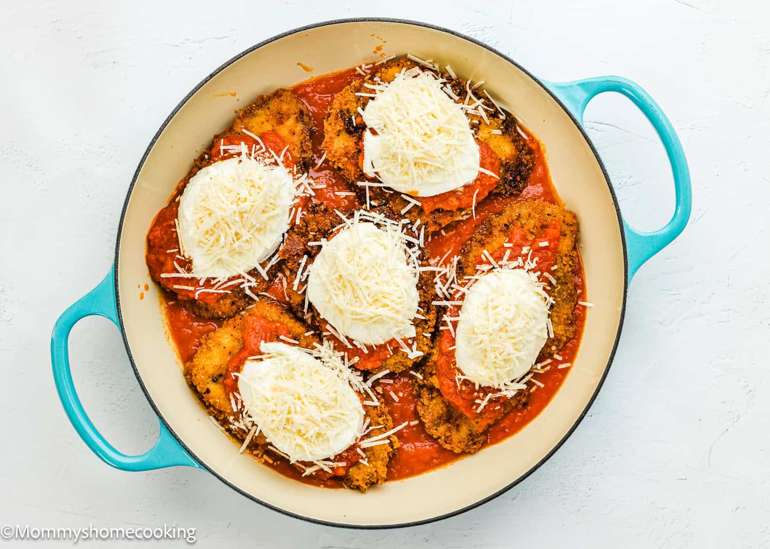 A round blue-handled baking dish filled with breaded Chicken Parmesan without Eggs, topped with tomato sauce, mozzarella, and shredded Parmesan cheese.