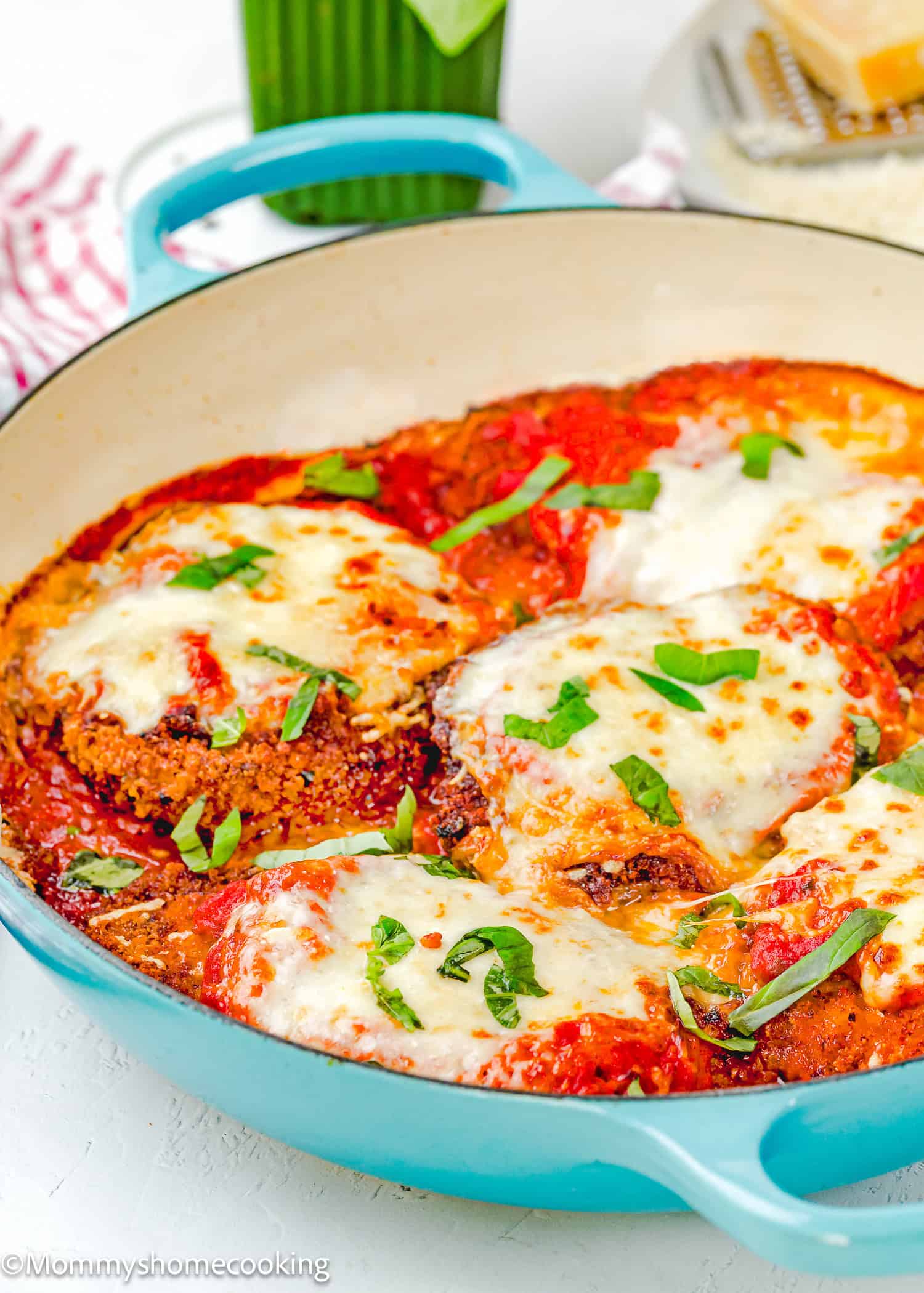 A cast iron skillet filled with Chicken Parmesan without Eggs—breaded chicken breasts topped with melted cheese, tomato sauce, and fresh basil.