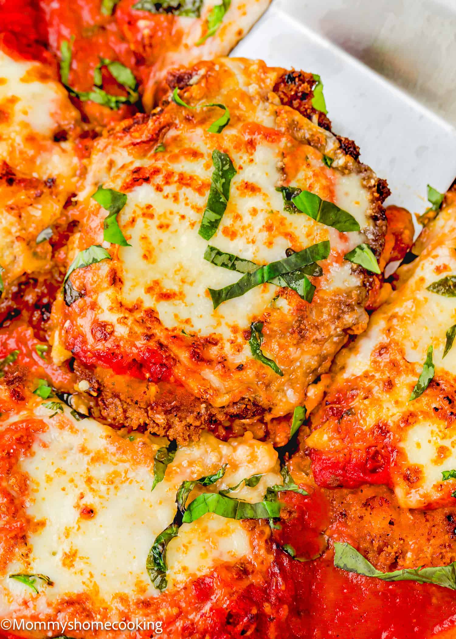 Close-up of Chicken Parmesan without Eggs: breaded chicken cutlets topped with melted cheese, tomato sauce, and fresh basil strips.