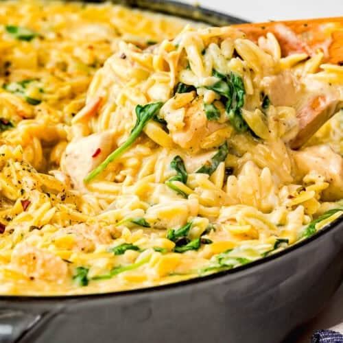 A close-up of creamy orzo pasta with spinach being stirred in a skillet with a wooden spoon, perfect as an Easy Lemon Chicken Orzo (One Pot) dish.