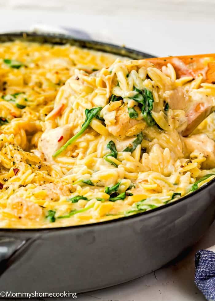 A close-up of creamy orzo pasta with spinach being stirred in a skillet with a wooden spoon, perfect as an Easy Lemon Chicken Orzo (One Pot) dish.