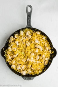 A black skillet filled with yellow rice, diced cooked chicken, and small pieces of onion on a white surface—perfect for fans of Easy Lemon Chicken Orzo (One Pot) dishes.