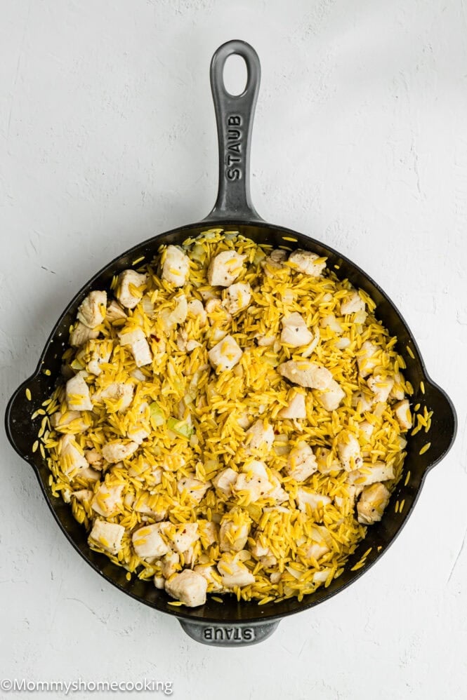 A black skillet filled with yellow rice, diced cooked chicken, and small pieces of onion on a white surface—perfect for fans of Easy Lemon Chicken Orzo (One Pot) dishes.