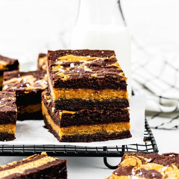 Three stacked Eggless Peanut Butter Brownies on a cooling rack, with a bottle of milk and more brownies in the background.