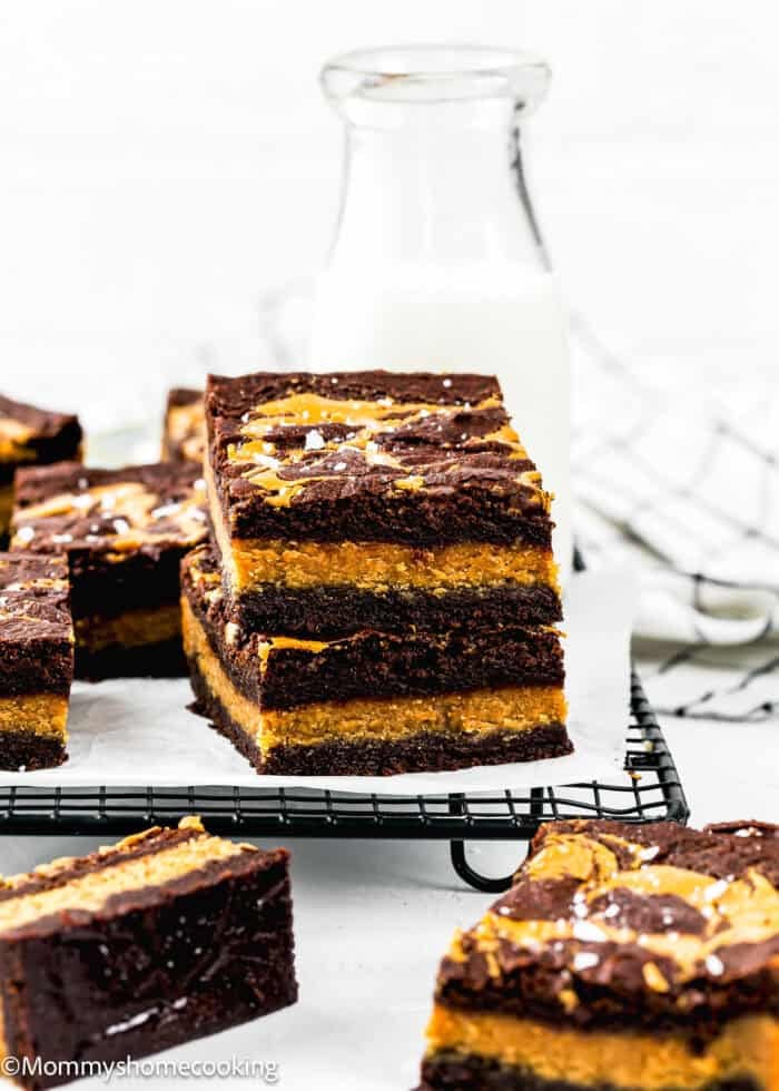 Three stacked Eggless Peanut Butter Brownies on a cooling rack, with a bottle of milk and more brownies in the background.