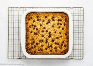 A square pan of Eggless Protein Baked Oatmeal topped with chocolate chips sits on a cooling rack against a white background.