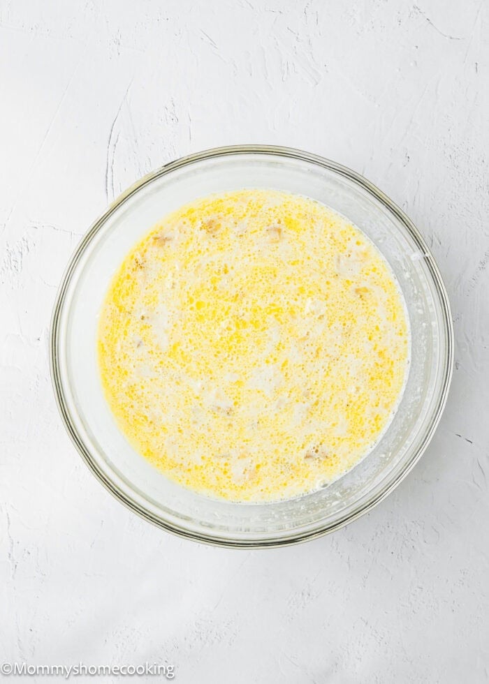 A clear glass bowl filled with a yellow and white liquid mixture, sitting on a light-colored textured surface.