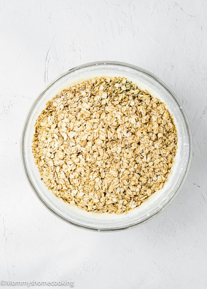 A glass bowl filled with rolled oats on top of a creamy mixture, set on a white textured surface.