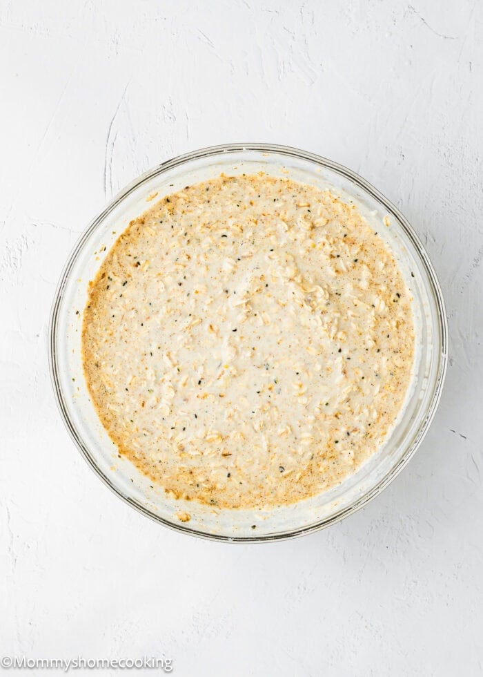 A clear glass bowl filled with a creamy, speckled dip mixture sits on a white textured surface.