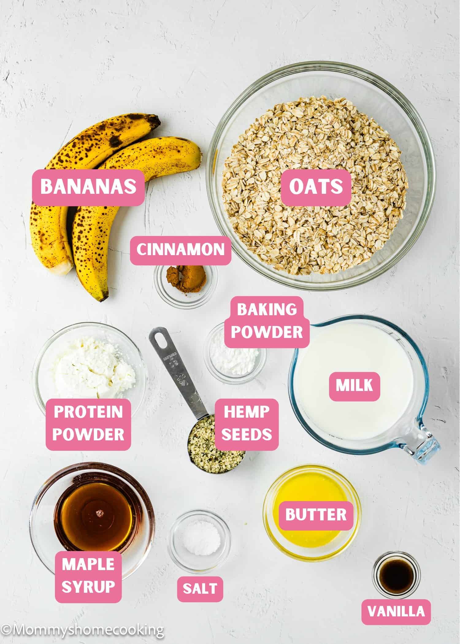 Top-down view of labeled ingredients of egg-free protein baked oatmeal: banana, oats, milk, butter, vanilla, maple syrup, salt, hemp seeds, cinnamon, protein powder, baking powder on a white background with pink text.