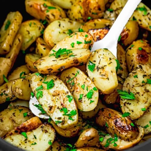 Roasted fingerling potatoes garnished with chopped parsley and herbs, reminiscent of Slow Cooker Lemon Greek Potatoes, served in a black dish with a white serving spoon.