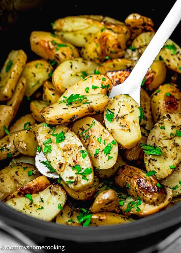Roasted fingerling potatoes garnished with chopped parsley and herbs, reminiscent of Slow Cooker Lemon Greek Potatoes, served in a black dish with a white serving spoon.