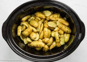 Slow Cooker Lemon Greek Potatoes: Fingerling potatoes seasoned with herbs, oil, and lemon in a black slow cooker, ready to be cooked.