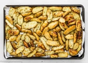 A baking sheet filled with roasted fingerling potatoes seasoned with herbs, inspired by Slow Cooker Lemon Greek Potatoes, and cooked to a golden brown.