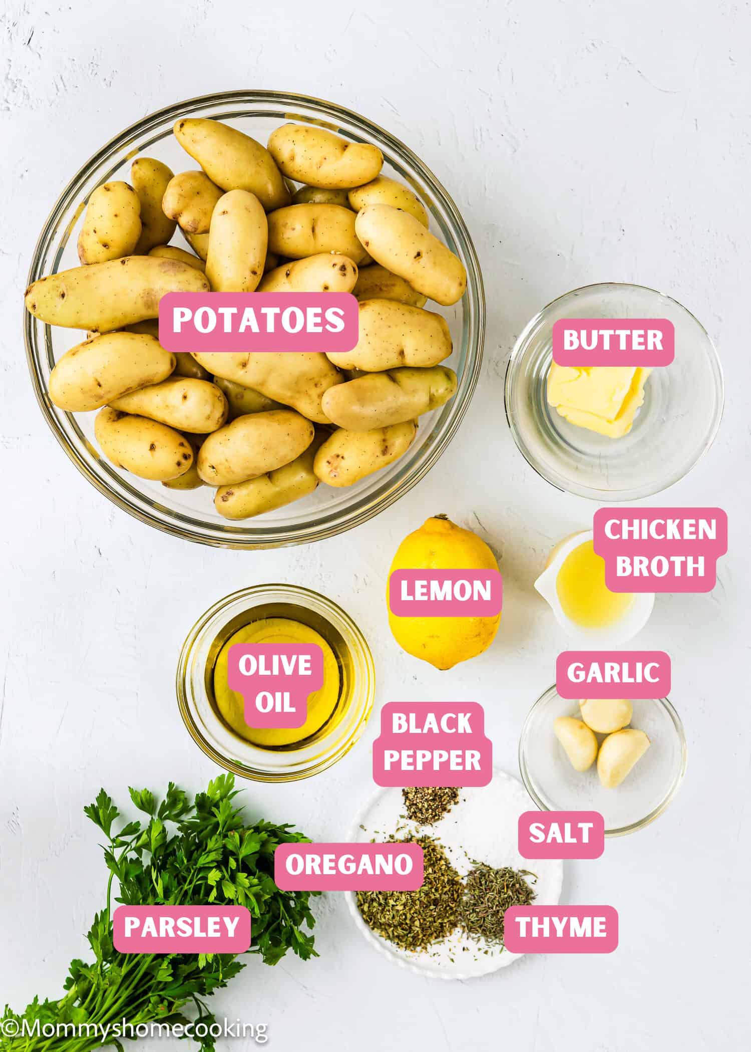 A bowl of fingerling potatoes and small bowls of butter, chicken broth, lemon, olive oil, garlic, black pepper, salt, oregano, thyme, and fresh parsley—perfect for making Slow Cooker Lemon Greek Potatoes.