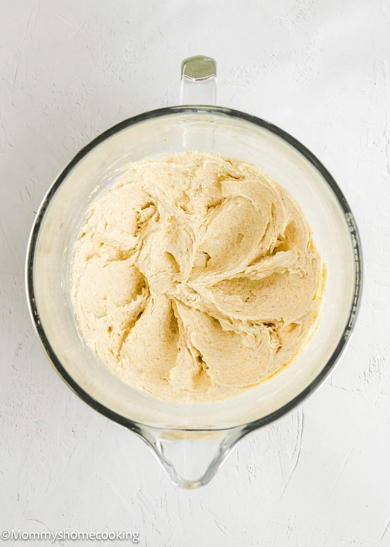 A glass mixing bowl filled with smooth, creamy cookie dough sits on a white surface.