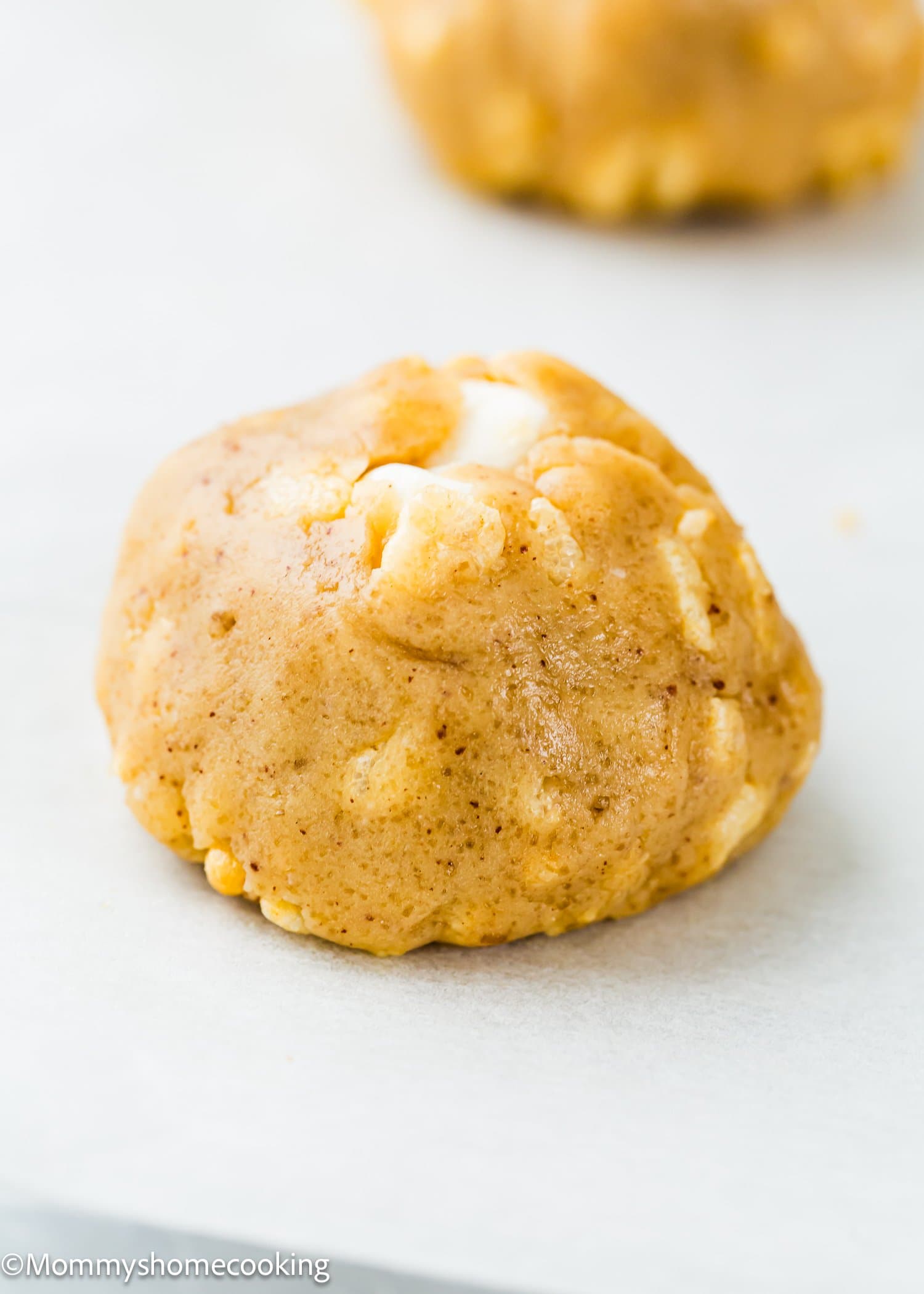 A close-up of an unbaked cookie dough ball with white chocolate chips on a parchment-lined surface.