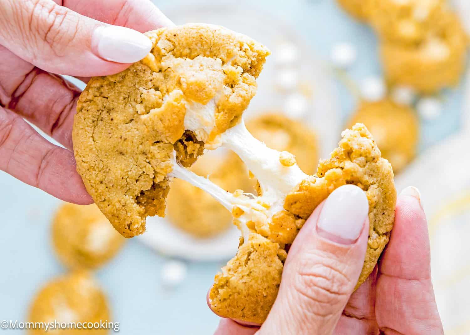 A person pulls apart an Easy Marshmallow Rice Crispy Cookie (Costco Copycat – Egg-Free), revealing melted marshmallow filling stretching between the two halves.