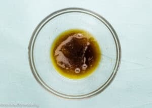 A clear glass bowl containing a mixture of melted butter and brown sugar on a light blue surface.