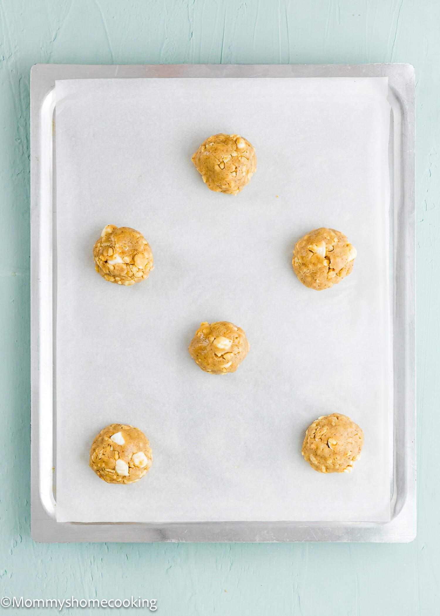 Six unbaked cookie dough balls are arranged on a parchment-lined baking sheet, ready to be baked.