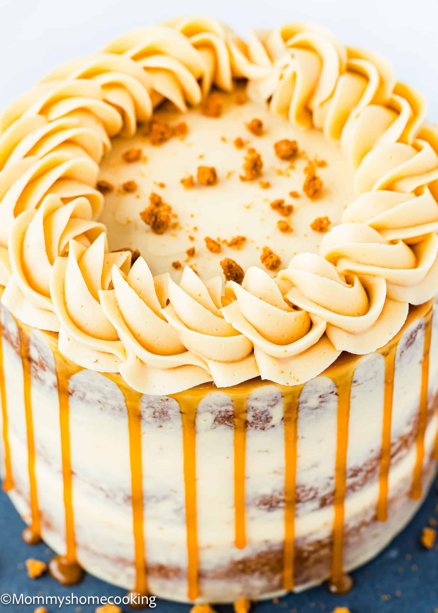 A layered cake with light frosting, caramel drizzle on the sides, piped swirls on top, and cookie crumbs sprinkled in the center.