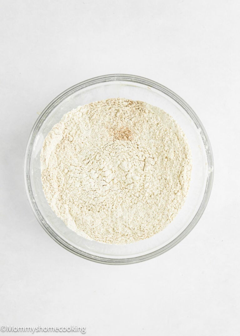 A clear glass bowl filled with dry flour on a white surface.