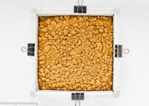 A square baking pan lined with parchment paper and binder clips holds a golden brown Egg-Free Pumpkin Coffee Cake with Crumb Topping, viewed from above.