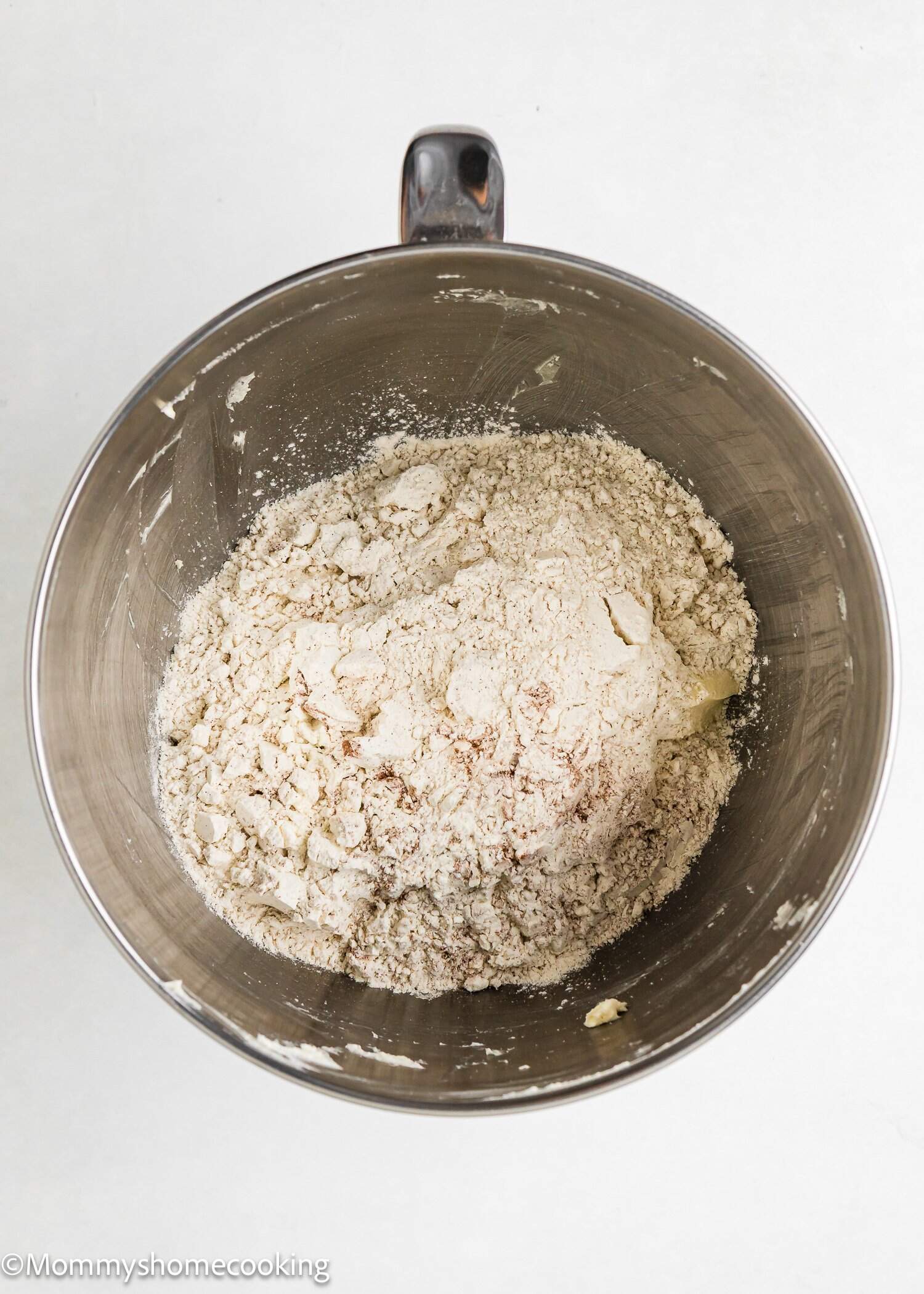 A metal mixing bowl containing a mixture of flour and other dry baking ingredients for Eggless Apple Pie Snickerdoodle Cookies rests on a white surface.
