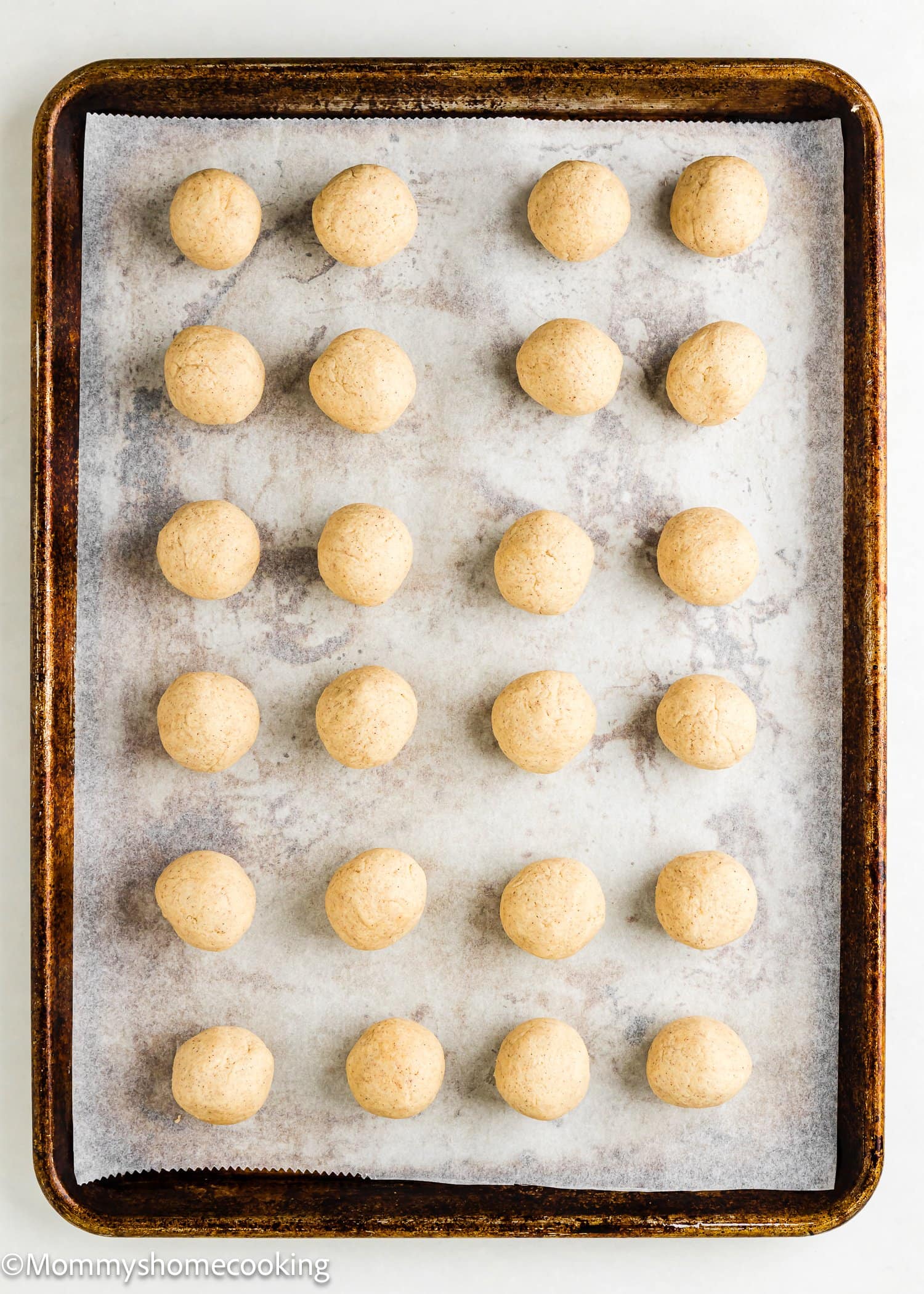 A baking tray lined with parchment paper holds 24 evenly spaced, unbaked Eggless Apple Pie Snickerdoodle Cookies dough balls arranged in a grid pattern.