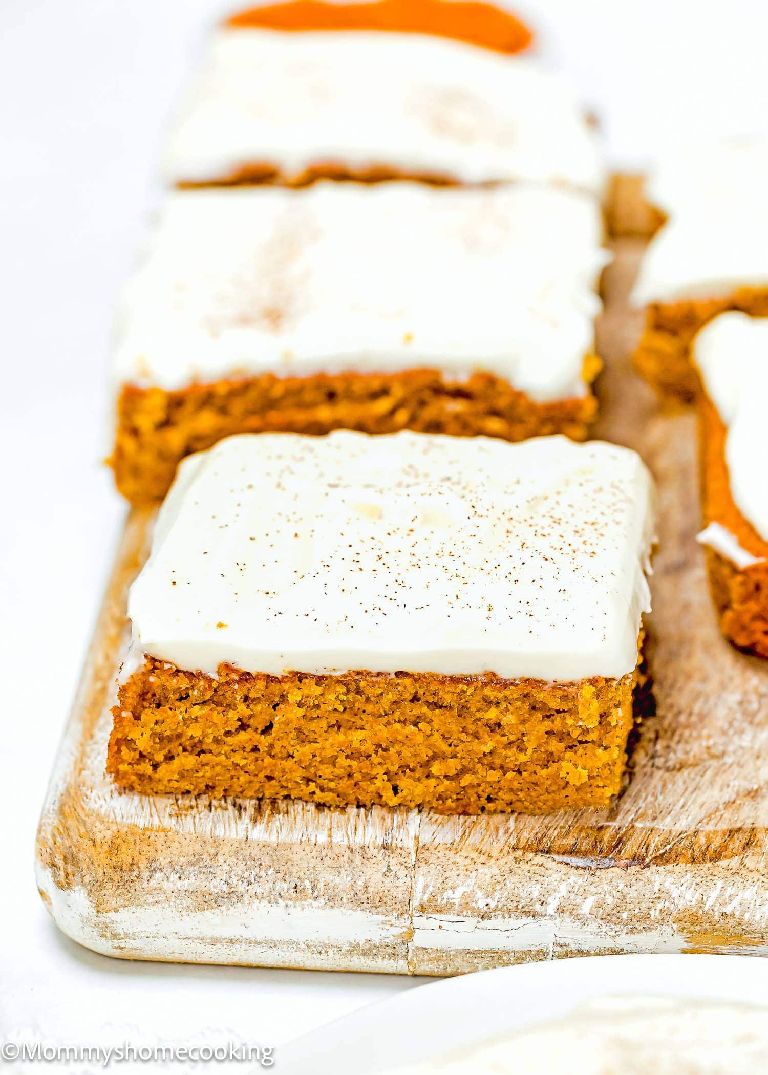 A close-up of pumpkin bars with cream cheese frosting, cut into squares and arranged on a wooden board—one of the 10 Easy Egg-Free Bar Recipes Every Baker Needs to try.