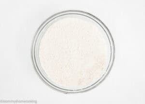 A clear glass bowl filled with white flour sits on a plain white surface.