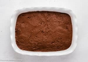 A rectangular white baking dish filled with unbaked chocolate cake batter sits on a white surface.
