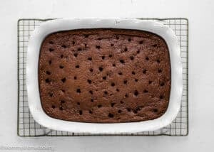 A rectangular chocolate cake with evenly spaced holes on top, baked in a white ceramic dish on a cooling rack.
