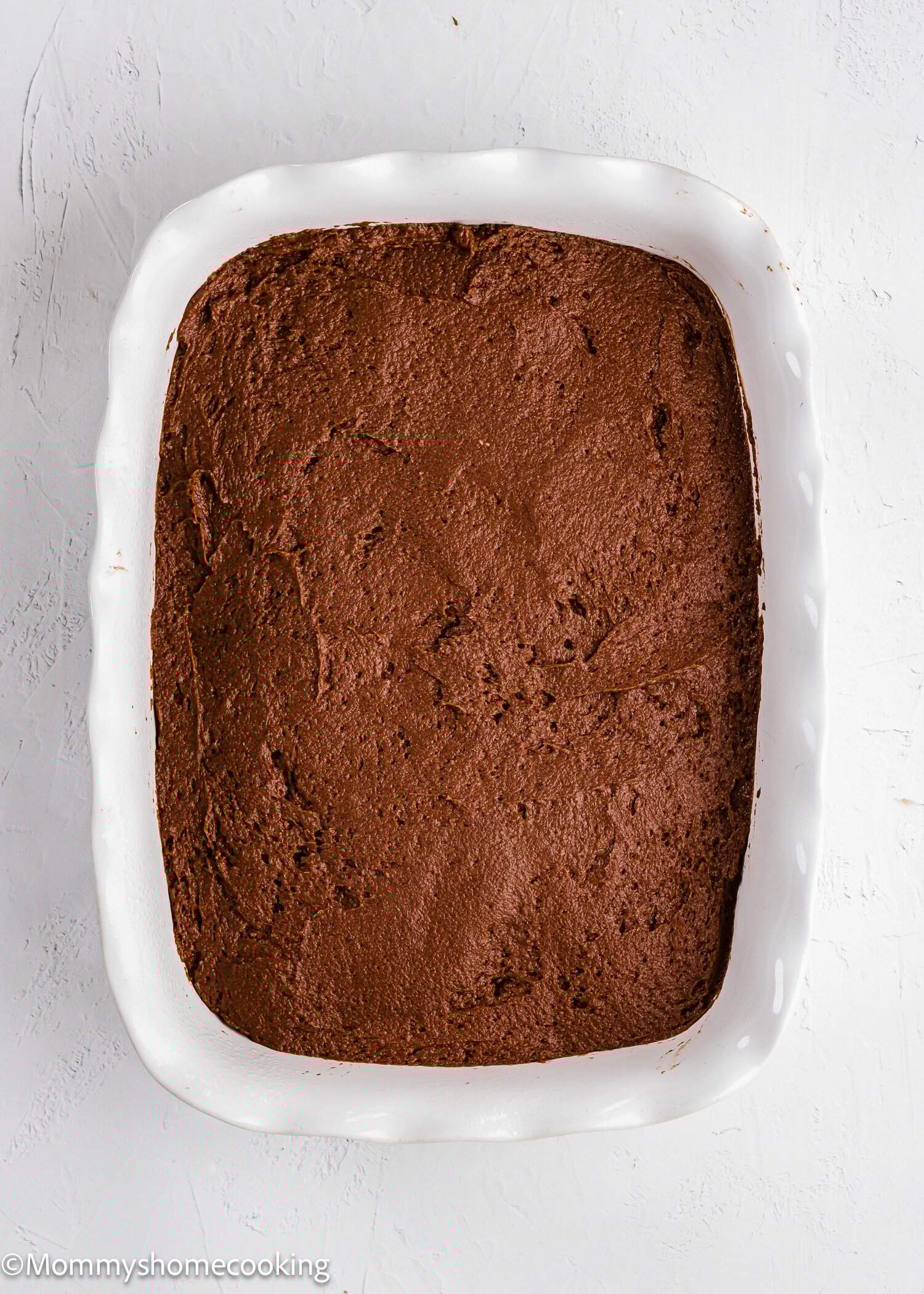 A white baking dish filled with an even layer of chocolate batter on a white surface.