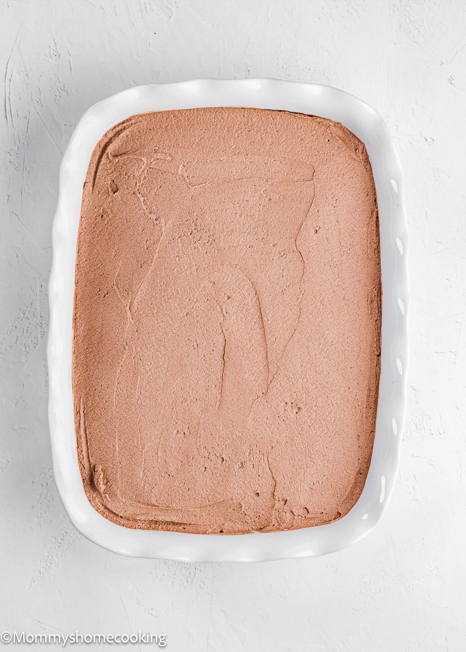 A white rectangular dish filled with a smooth layer of light brown mousse or whipped dessert, viewed from above on a white surface.