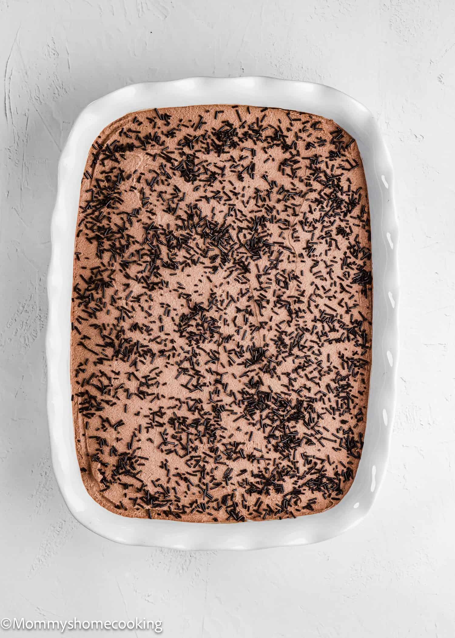 A rectangular white baking dish filled with a chocolate dessert topped with chocolate sprinkles, placed on a light-colored surface.