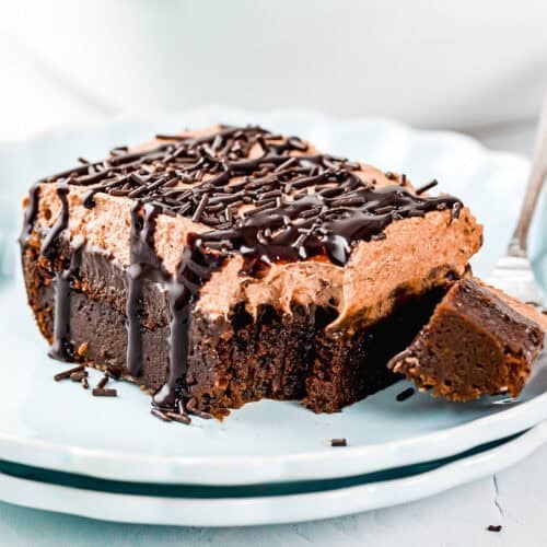 A slice of chocolate mousse cake topped with chocolate sprinkles and sauce sits on a plate, with a fork holding a small bite.