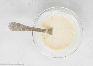 A bowl of pancake batter with a silver spoon resting inside, placed on a light gray surface—perfect for pairing with savory treats like Garlic Parmesan Chicken Bites.