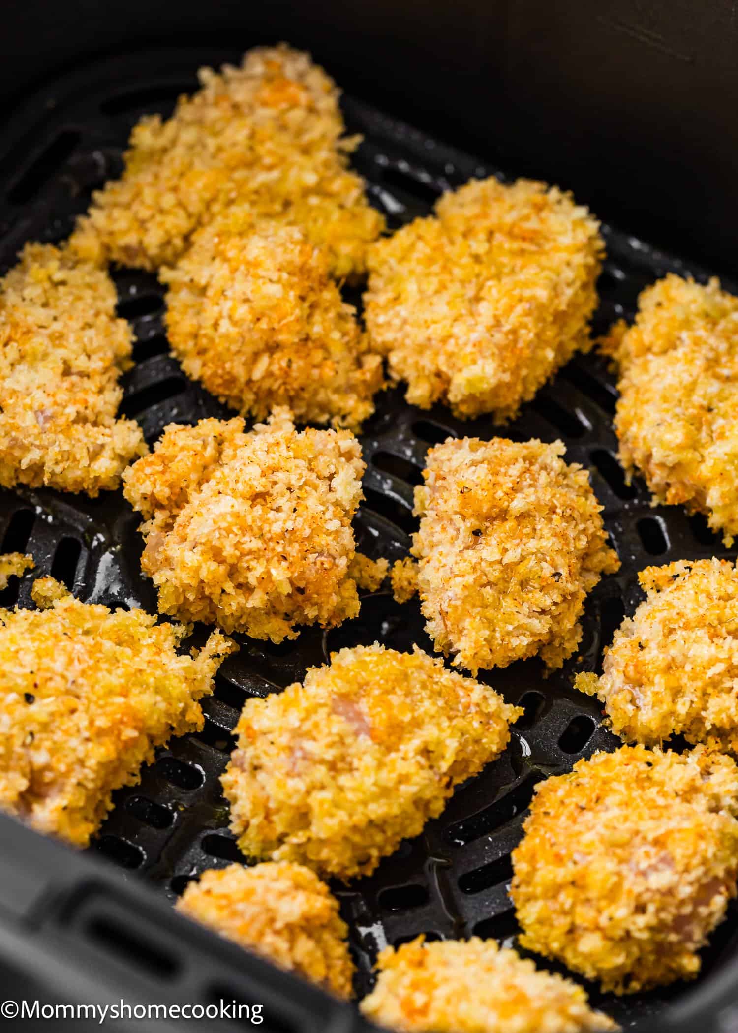 Close-up of several golden, crispy Garlic Parmesan Chicken Bites arranged in a black air fryer basket. The nuggets look crunchy and freshly cooked, with a textured coating.