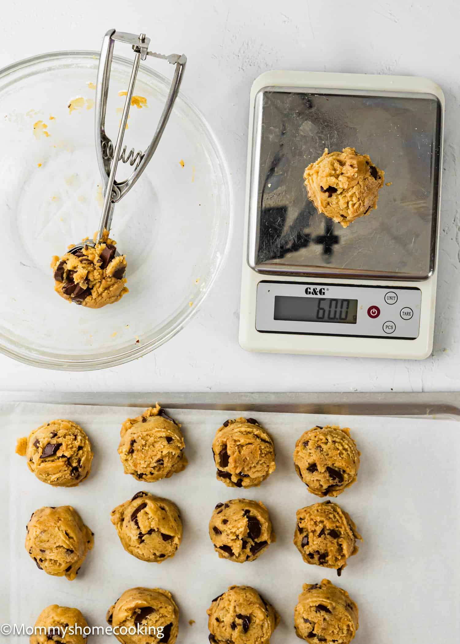 Overhead view of cookie dough balls on a baking sheet, a digital scale showing 60 grams with a dough ball on it, an empty glass bowl, and a cookie scoop containing dough.
