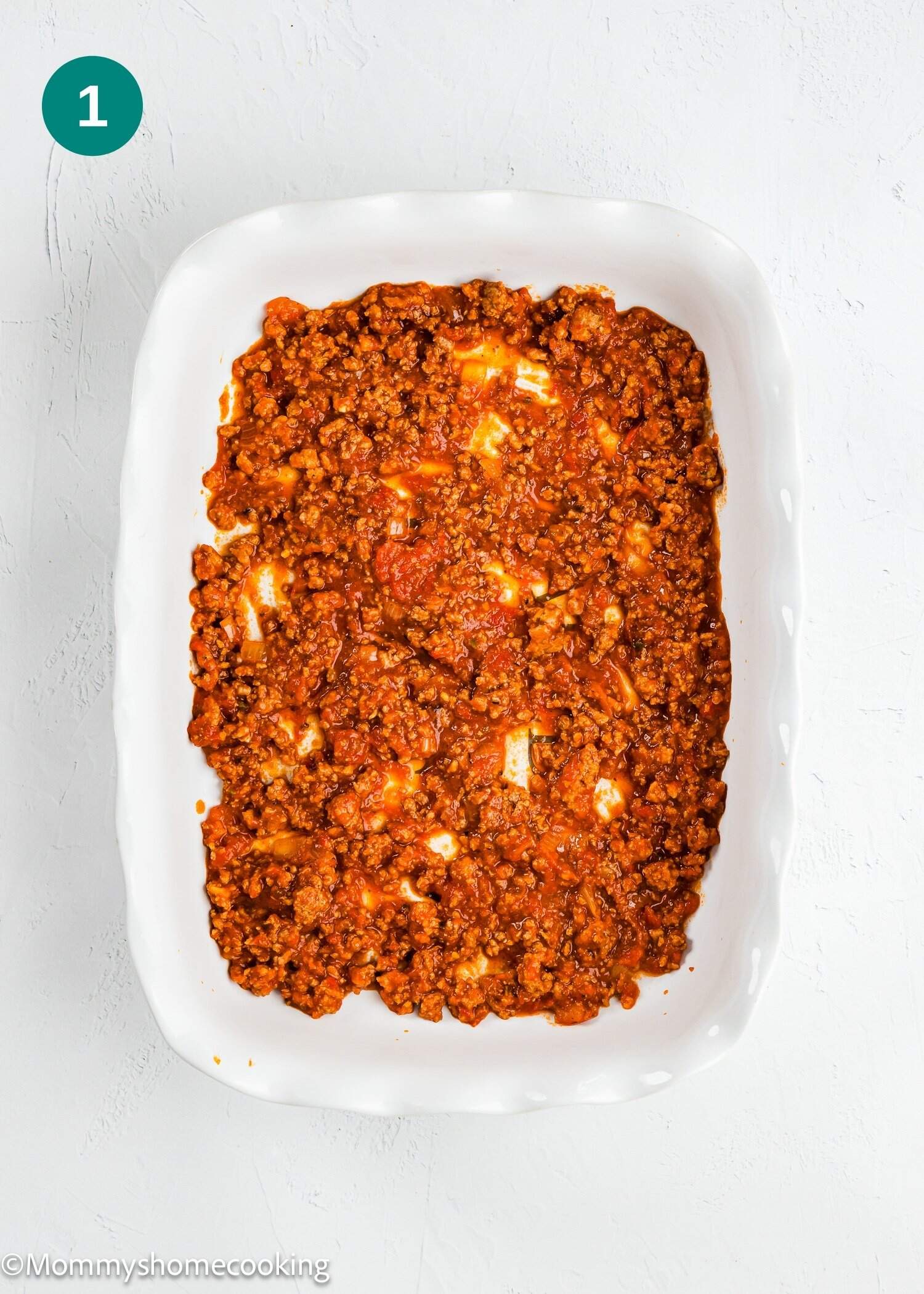 A white baking dish filled with cooked ground meat in red tomato sauce, spread evenly.