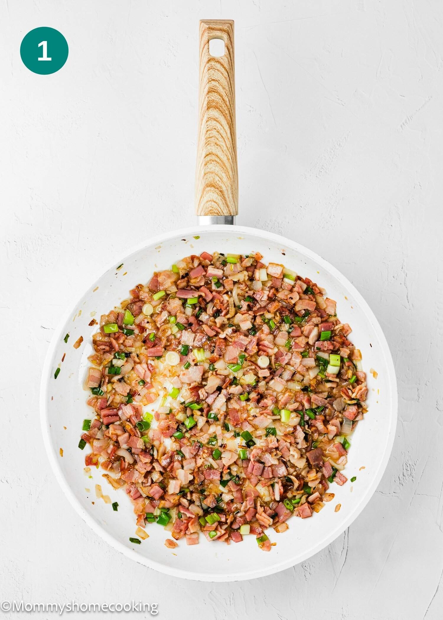 A white skillet filled with sautéed diced bacon, onions, and green onions on a light surface—perfect as a filling for Eggless Bacon and Cheese Quiche.