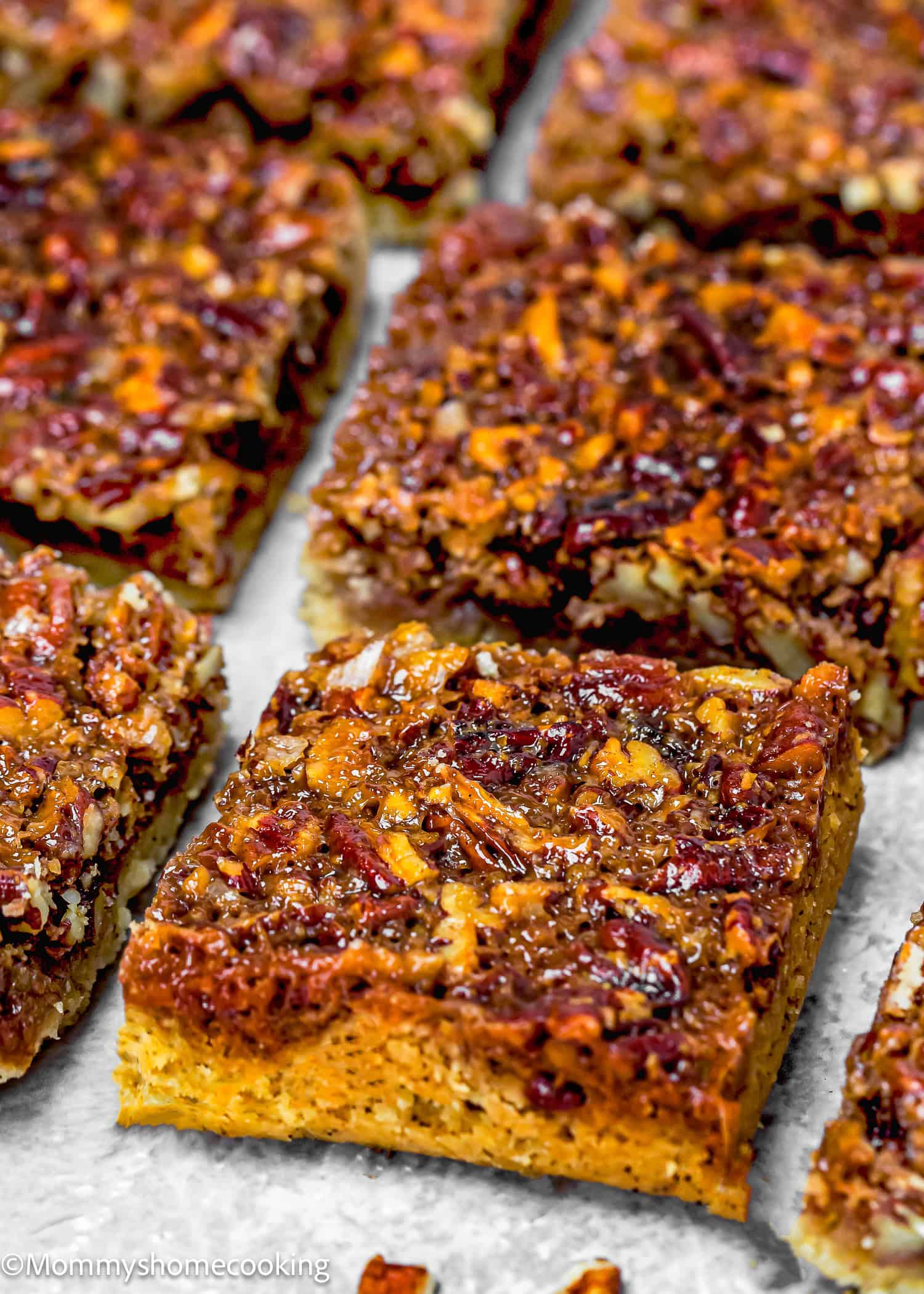 Close-up of eggless brown butter pecan pie bars. The golden crust and nutty caramelized topping are arranged on a cookie sheet.