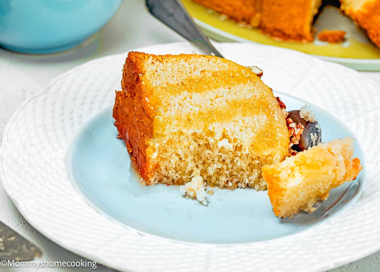 A slice of Eggless Butter Rum Bundt Cake with cream filling sits on a white plate, with a portion of the cake cut and lying next to it.